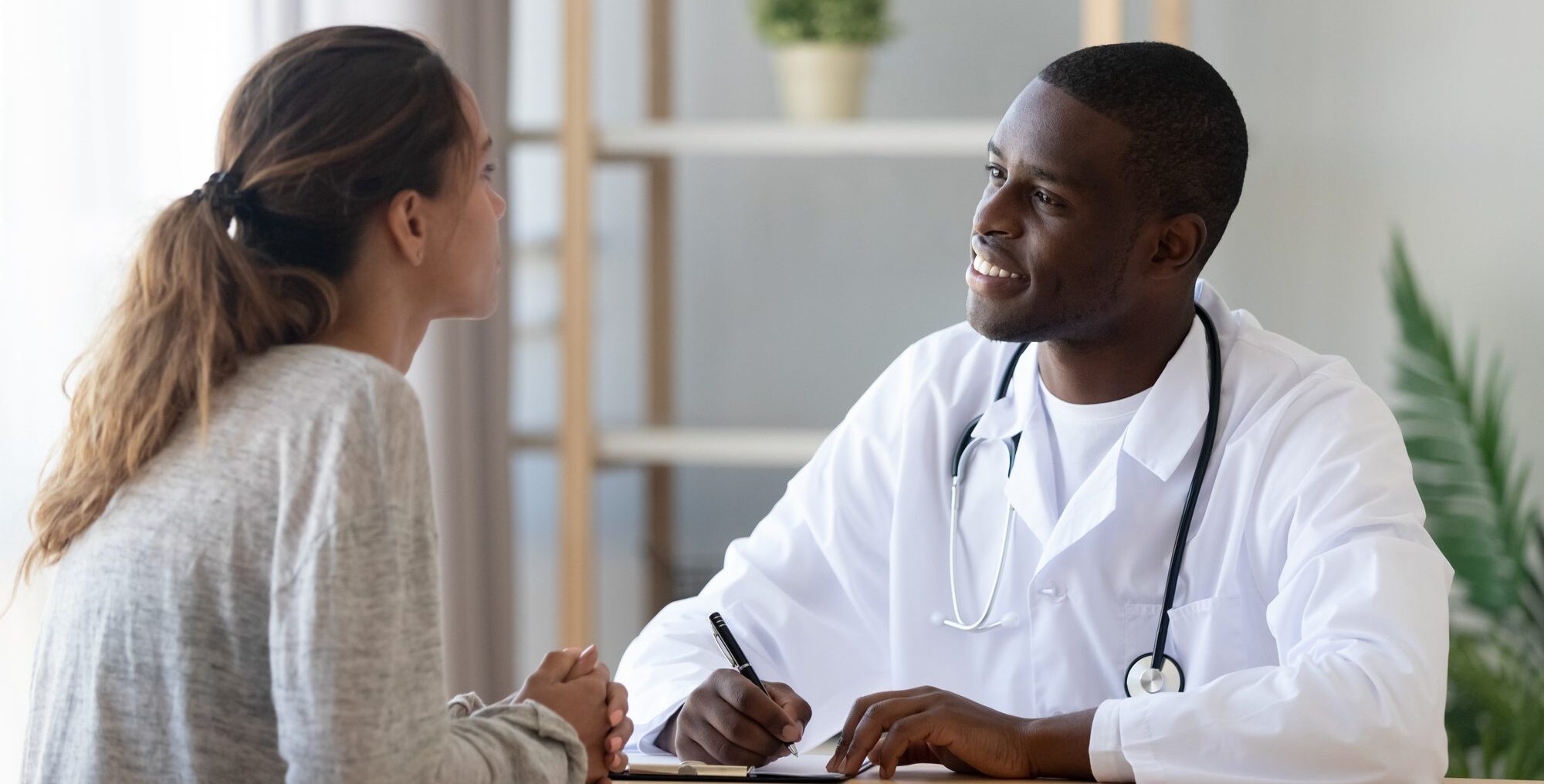 Young Caucasian Woman Talking to Smiling African Black Male Doctor